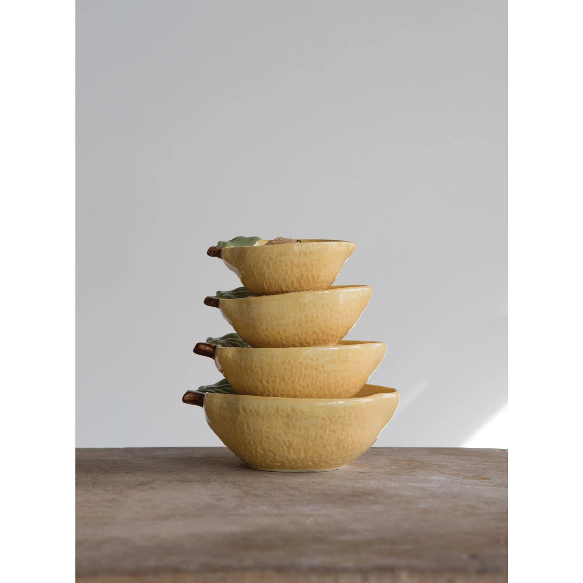 Set of four cream-colored stoneware lemon-shaped measuring cups with black handles.
