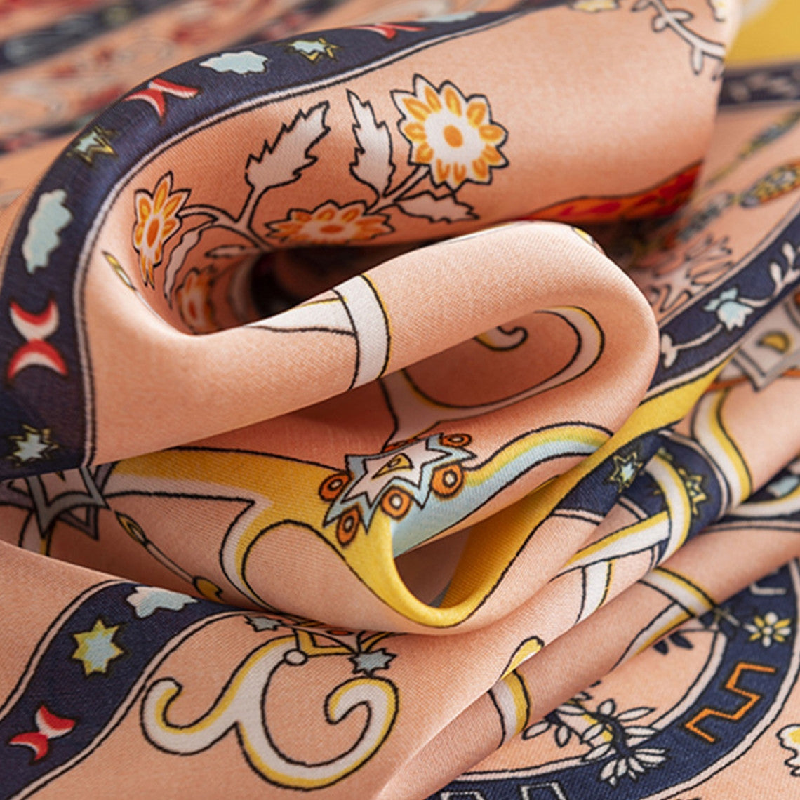 Close-up of a folded peach floral satin square scarf with intricate blue and yellow patterns.