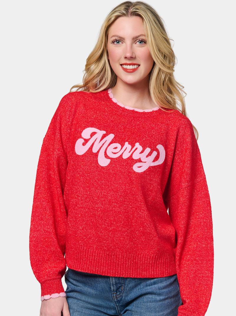 Woman wearing a red relaxed sweater with pink scalloped trim and pink retro 'Merry' lettering.