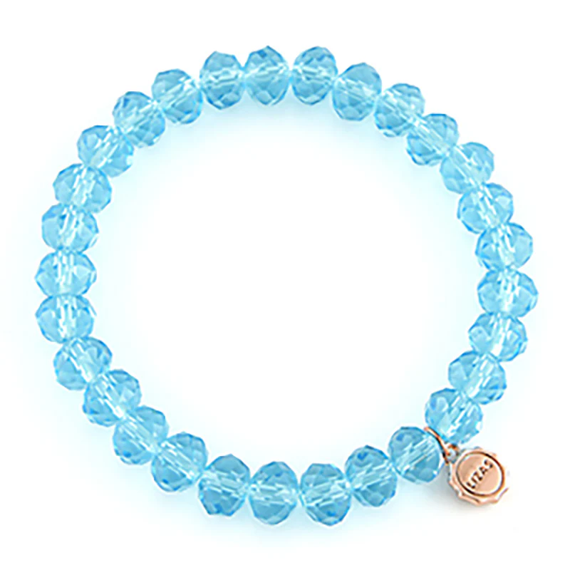 Lizas Quadro Big light blue faceted crystal bead stretch bracelet with a small gold logo charm.