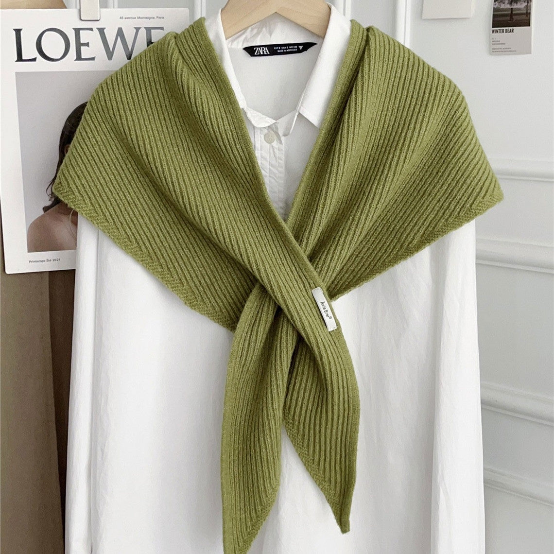 Green knitted solid cross triangle shawl draped over a white button-down shirt on a hanger.