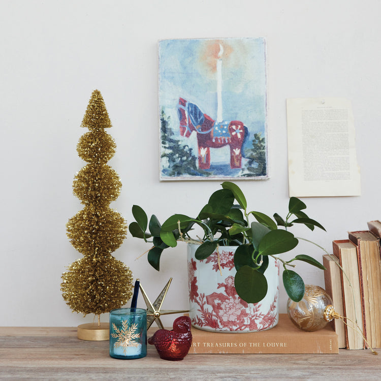 Hand-painted stoneware planter with red floral patterns holding a green leafy plant on a shelf.