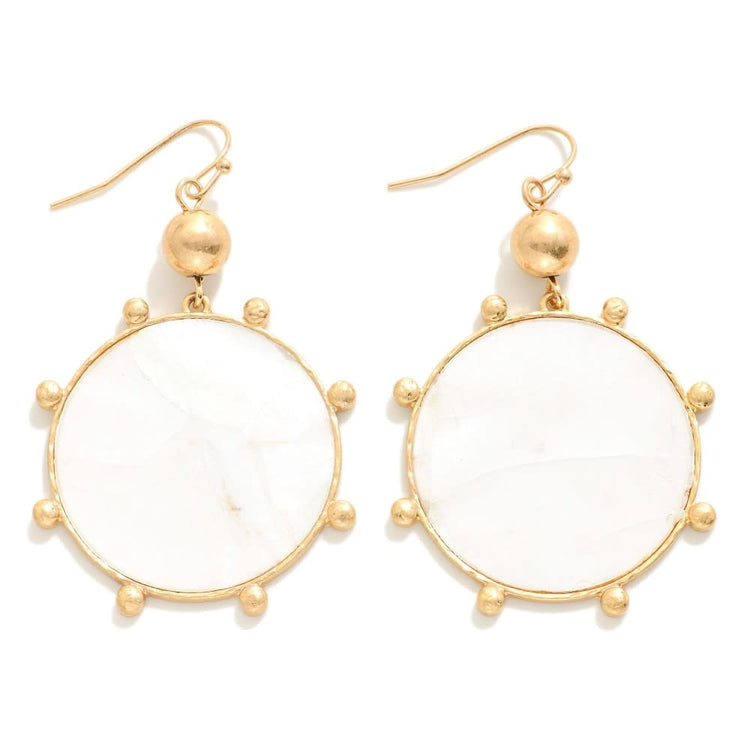 White pearlescent circle drop earrings with a gold tone studded border.