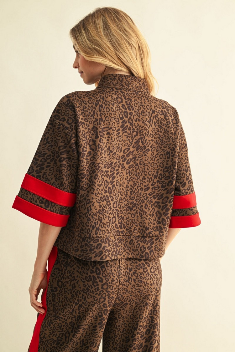 Back view of a woman wearing a leopard print faux suede top with red striped sleeve details.