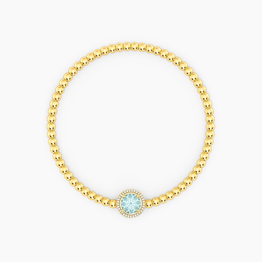 Gold plated beaded bracelet with a round-cut light blue gemstone and diamond halo charm.