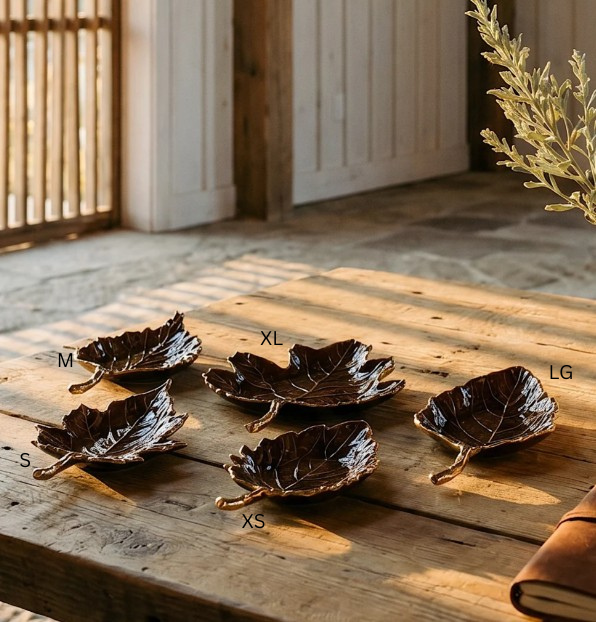 Five brown enamel leaf-shaped trays in various sizes with gold stems on a rustic wooden table.