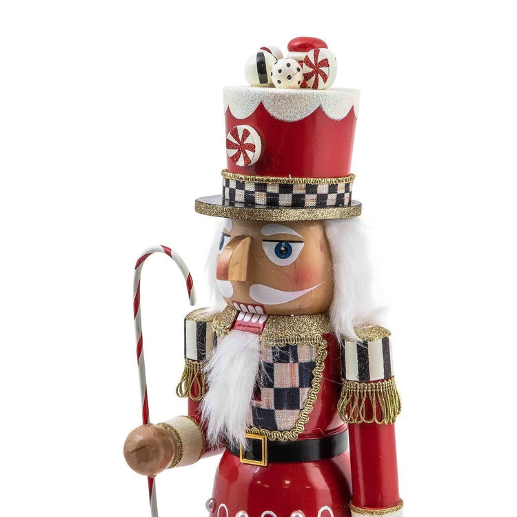 Hand-painted wooden peppermint nutcracker in red Courtly Check fabric holding a candy cane with scattered peppermints.