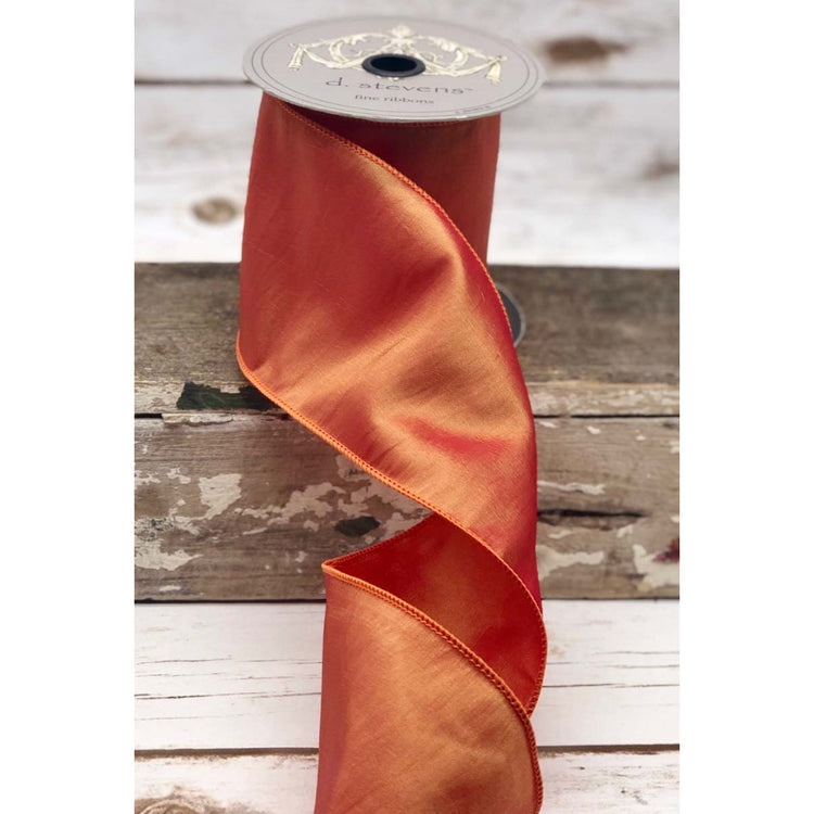 4-inch wide pink-gold iridescent taffeta ribbon on a spool, draped over a rustic wooden surface.