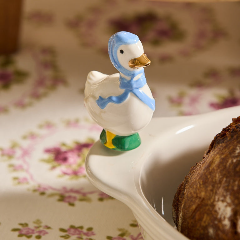 Hand-painted Porch Pal goose mini figurine wearing a blue bonnet and scarf on a white dish.