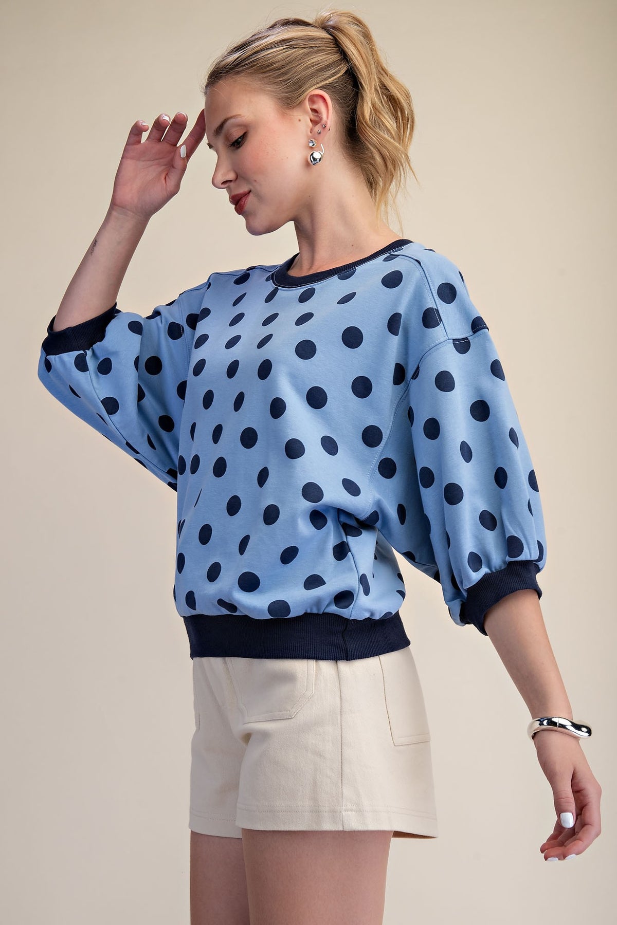 Woman wearing a light blue polka dot sweatshirt with bubble sleeves and cream shorts.
