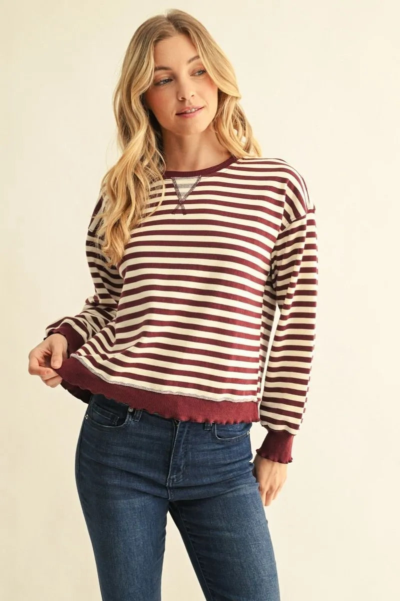 Woman wearing the Arya burgundy and cream striped long sleeve French terry sweatshirt with jeans.