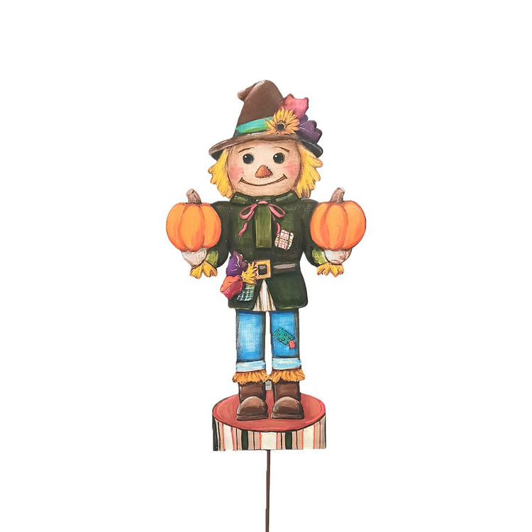 Small scarecrow nutcracker figure holding two pumpkins, wearing a brown hat and green jacket.