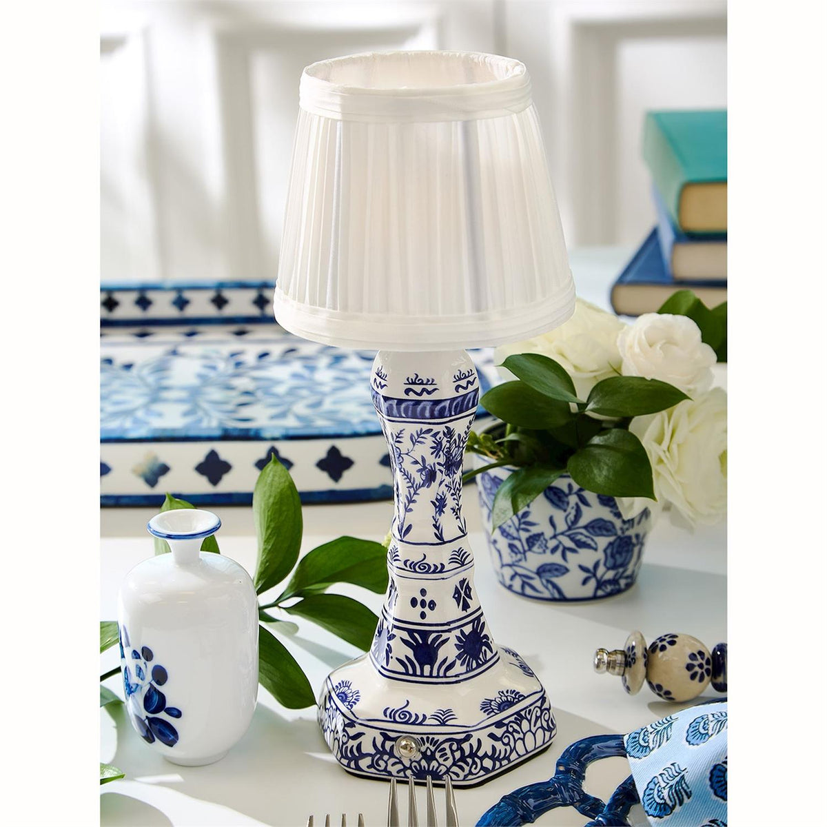 Cordless blue and white chinoiserie ceramic table lamp with a white pleated shade on a table.