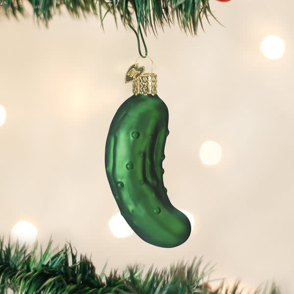 Green glass pickle ornament with gold stem hanging on a Christmas tree branch.