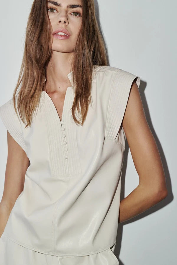 Woman wearing a Melissa sleeveless vegan leather blouse in cream with a split neck and cap sleeves.