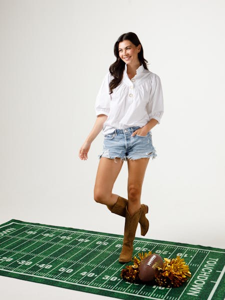 Woman wearing the white Avie Top with a stand collar, denim shorts, and brown boots.