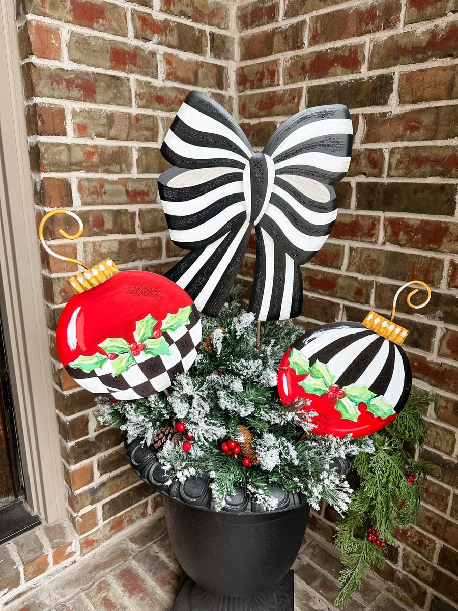 Black and white striped bow with red and black checkered ornaments with holly, in a flocked greenery arrangement.