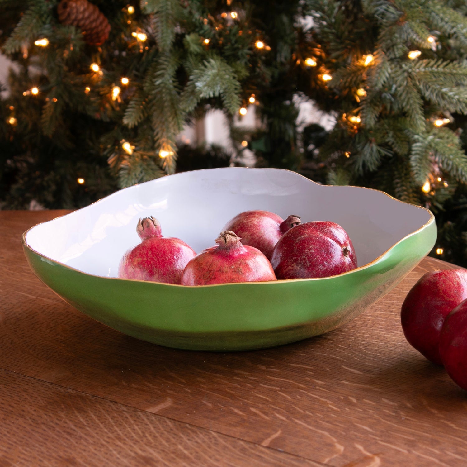 Encanto Nuevo large leaf green and white bowl with gold rim holding pomegranates on a wooden table.