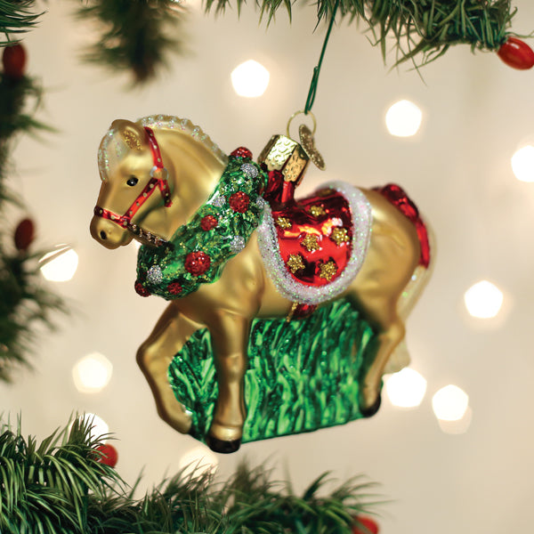 Golden horse ornament with a green wreath and red saddle hanging on a Christmas tree.