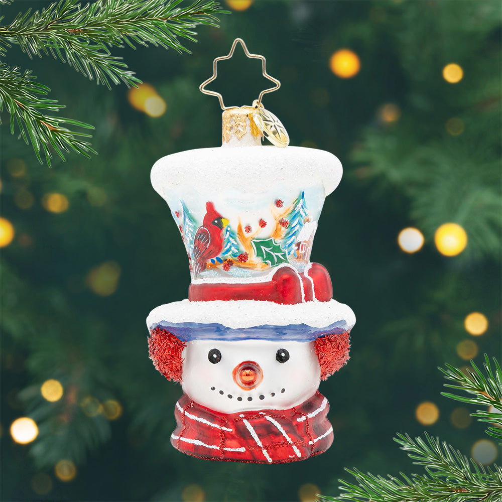 Snowman ornament with a cardinal winter scene on his top hat, wearing a red scarf and earmuffs.