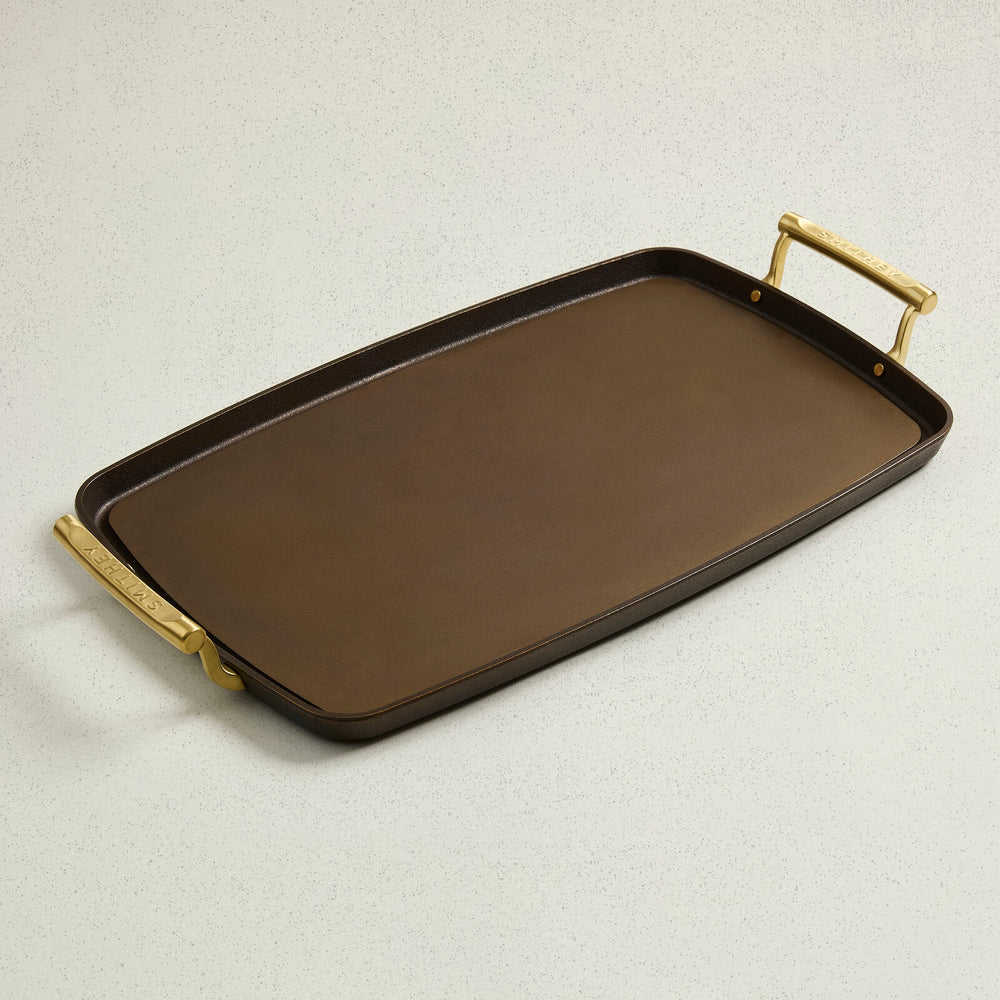 Rectangular cast iron double burner griddle with smooth cooking surface and brass handles.