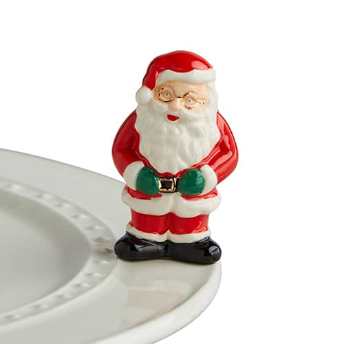 Ceramic Father Christmas figurine with red suit, white beard, and black boots, perched on the edge of a white plate.