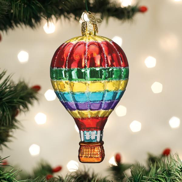 Vibrant rainbow-striped glass hot air balloon ornament hanging on a Christmas tree.