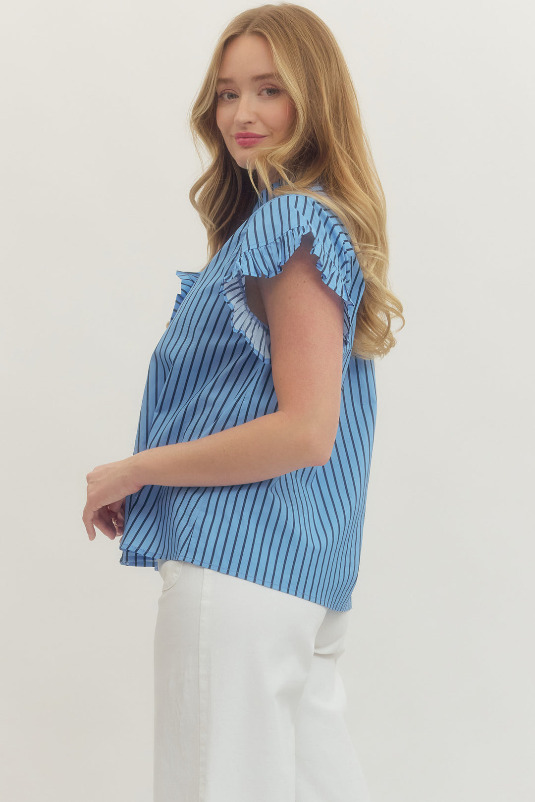 Woman wearing a blue and black Rhea Striped Short Sleeve Top with ruffle sleeves and white pants.