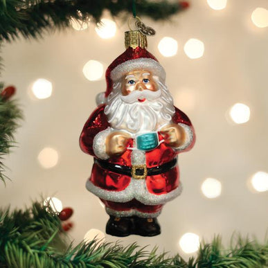 Santa Revealed glass ornament hanging on a Christmas tree, holding a small blue face mask.