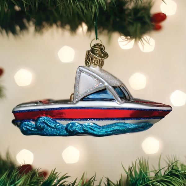 Hand-painted glass ski boat ornament with red, white, and blue glitter details hanging on a tree.