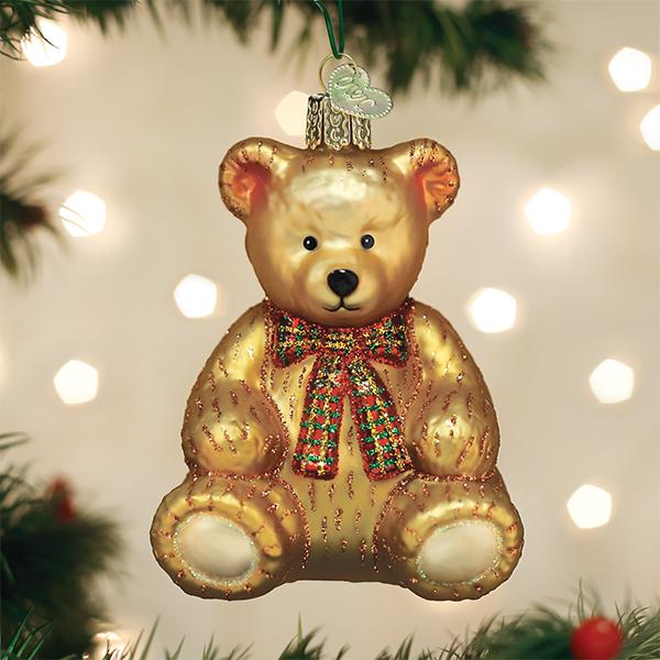 Golden glass teddy bear ornament with a red and green plaid bow, hanging on a Christmas tree.