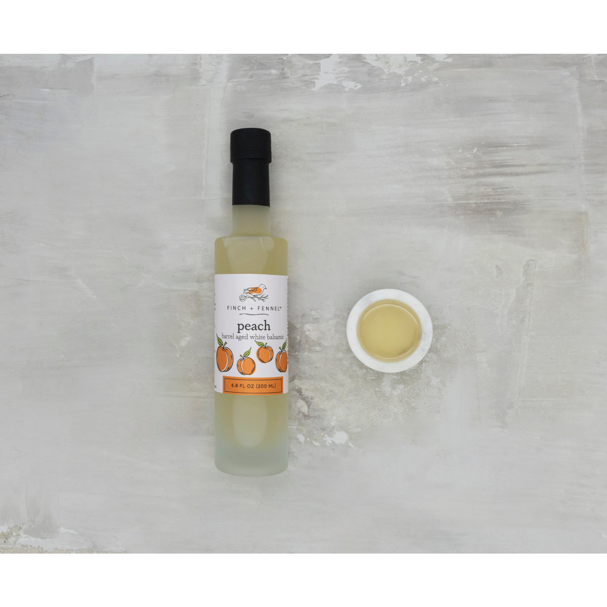 6.8 oz bottle of peach barrel aged white balsamic vinegar with a clear glass silhouette and gold cap.