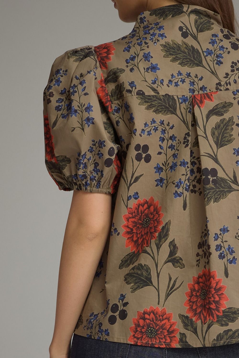 Back view of a woman wearing a khaki floral top with red flowers and short puff sleeves.