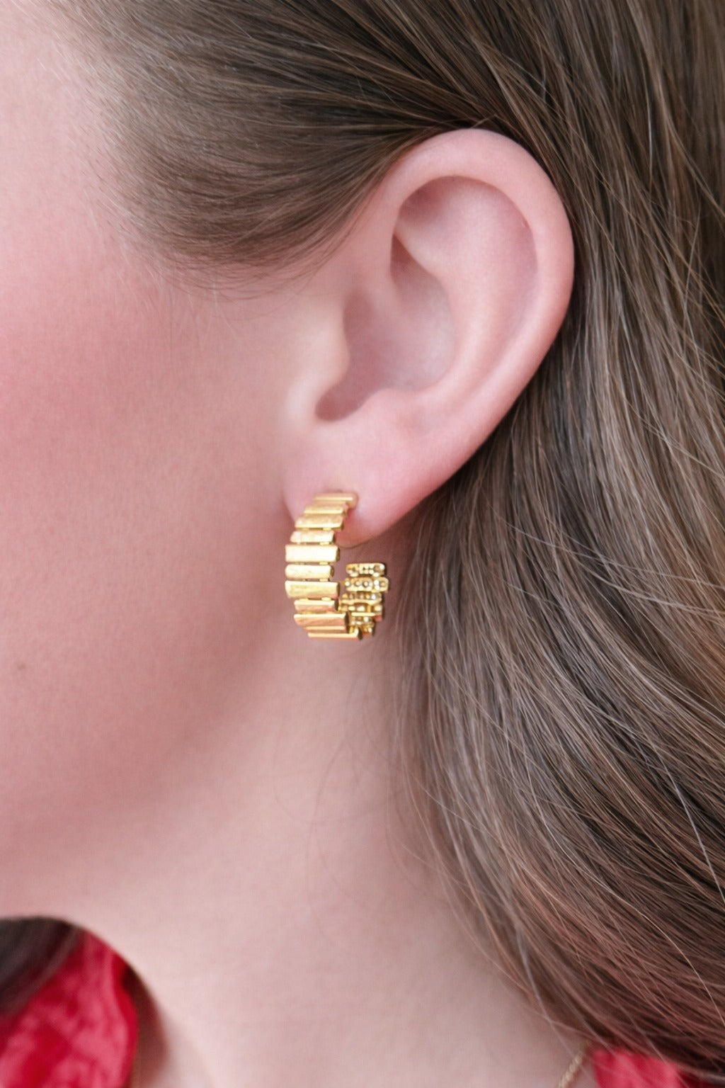 Close-up of a person wearing a gold WS Hollis Hoop Earring with a textured, ribbed design.