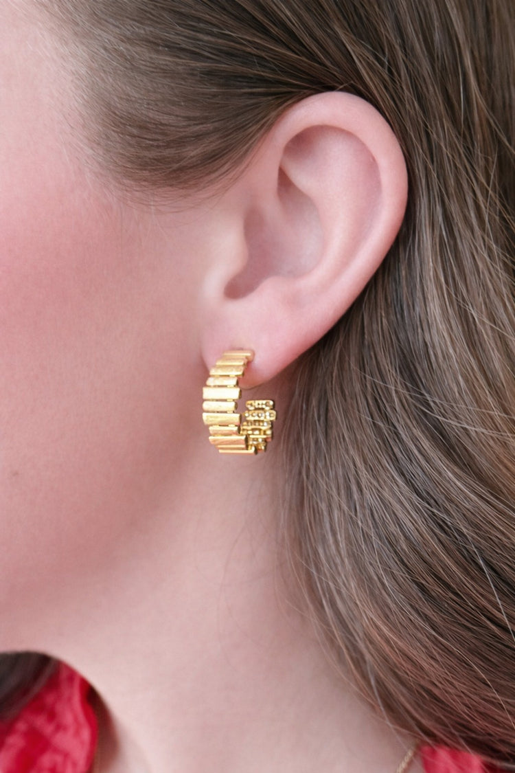 Close-up of a person wearing a gold WS Hollis Hoop Earring with a textured, ribbed design.