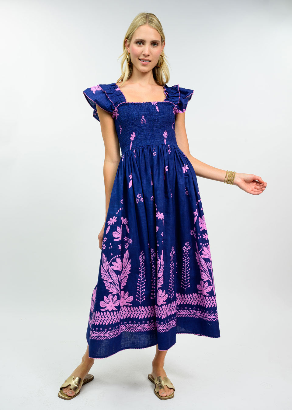 Woman wearing the Celine Smocked Border Print Dress in navy blue with pink floral patterns.