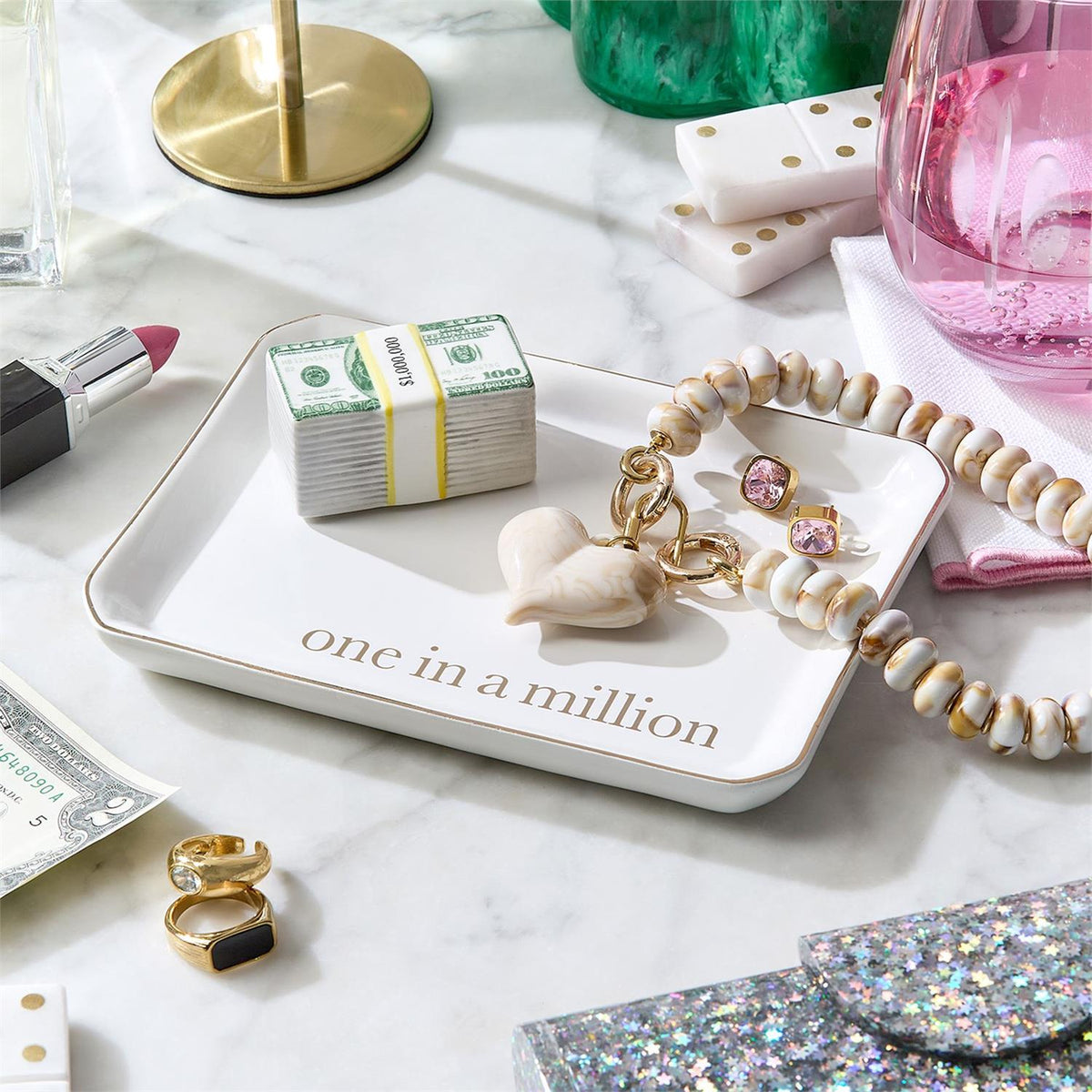 White ceramic trinket tray with gold foil 'one in a million' text, holding jewelry and accessories.