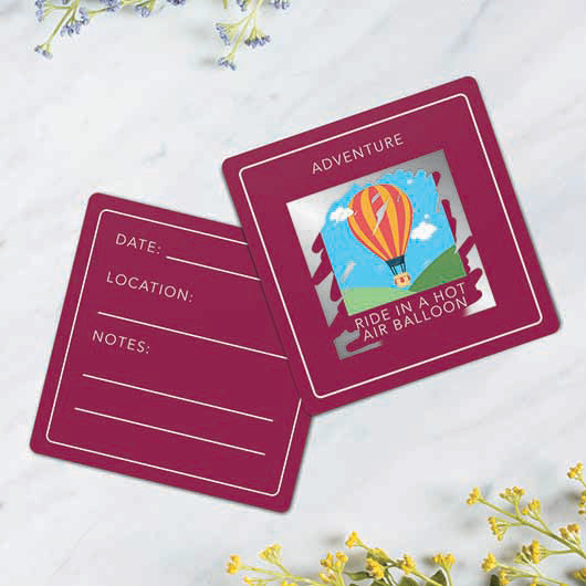 Two maroon scratch cards from the 'Things to do before your 50' pack, showing a hot air balloon.