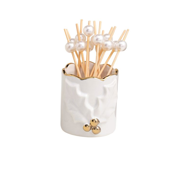 White stoneware toothpick caddy with gold trim and holly motif, holding pearl-topped toothpicks.