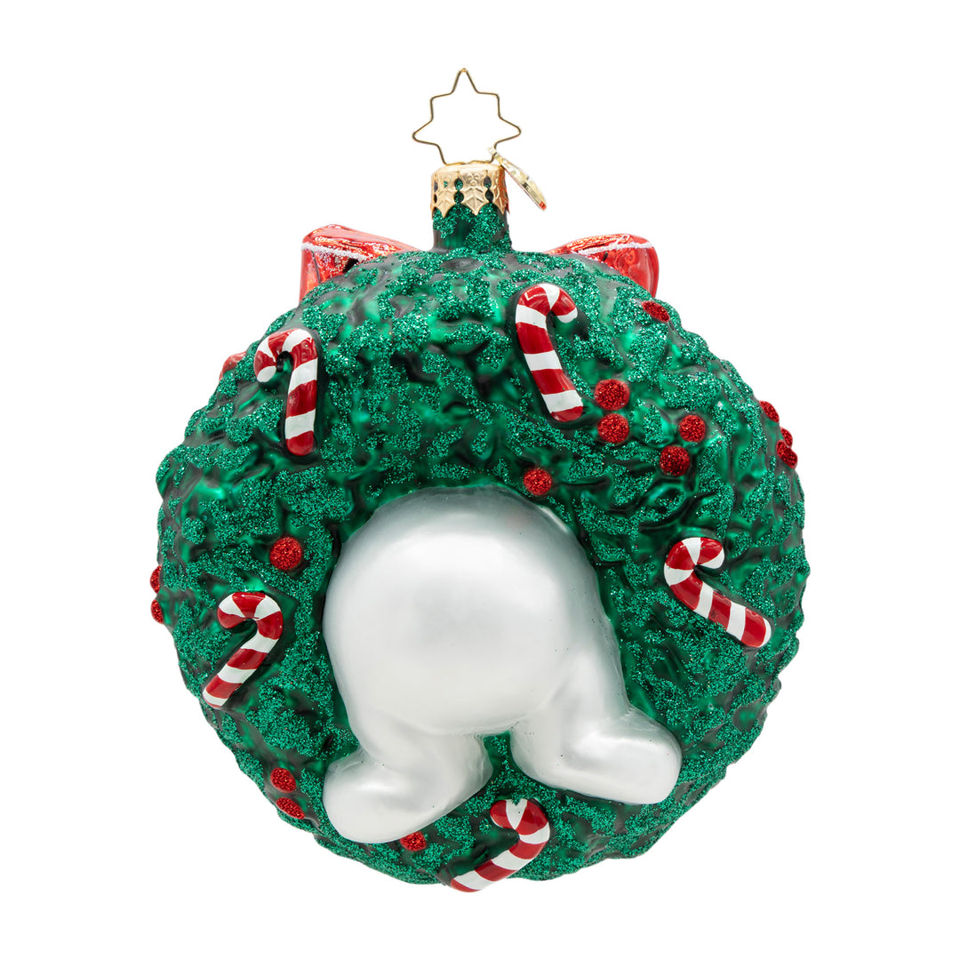 Snowman bottom tucked inside a green glitter wreath ornament with candy canes and red berries.