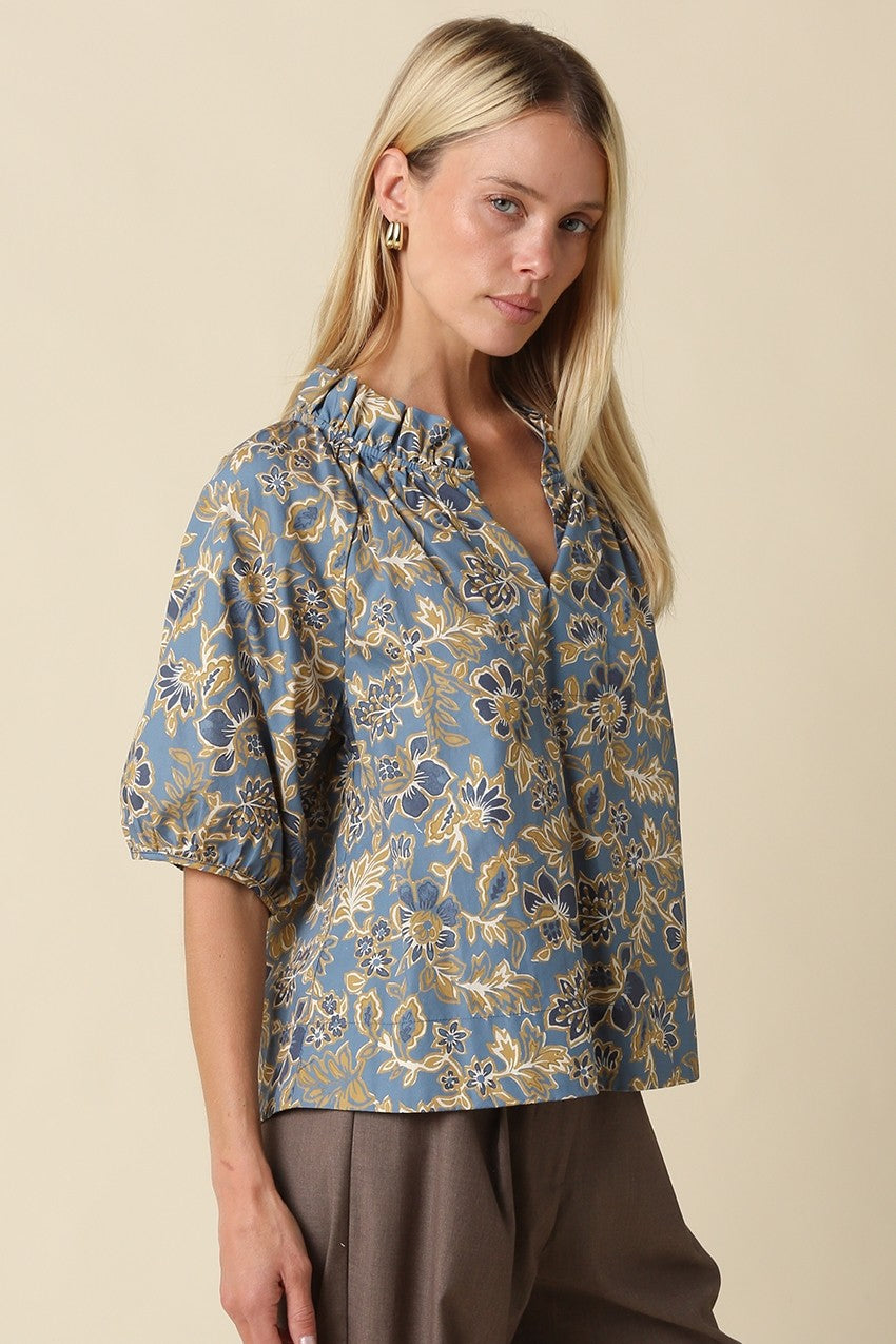 Woman wearing the Marina Floral Puff Sleeve Blouse in blue with a ruffled neckline.