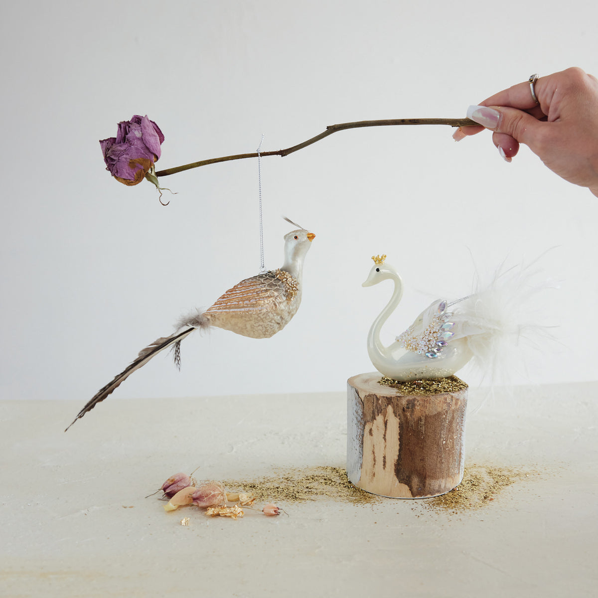 Hand-painted glass swan ornament with a gold crown and white feathers on a wooden pedestal.