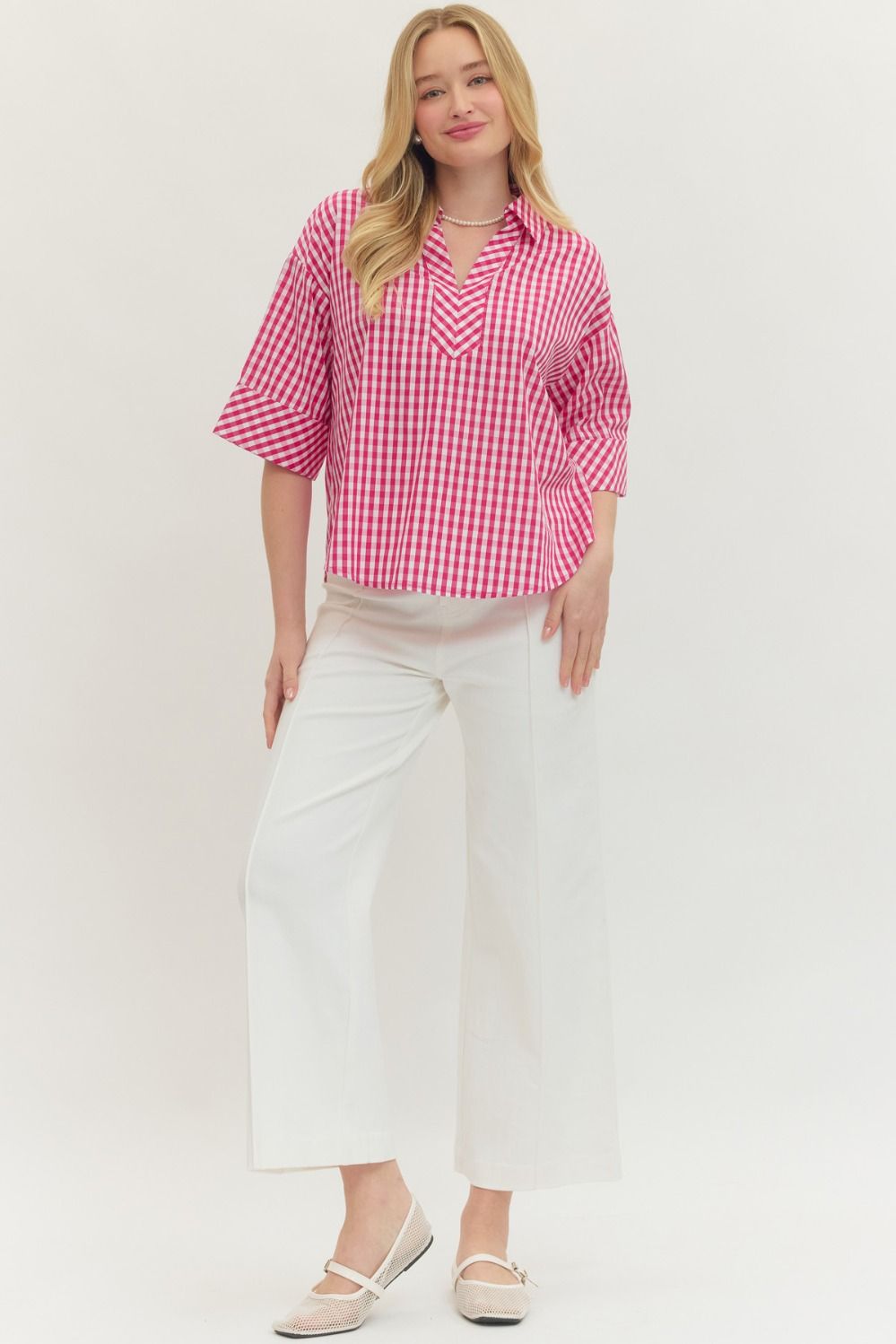 Woman wearing a pink and white Pamela Gingham Print ¾ Sleeve Top with white wide-leg pants.