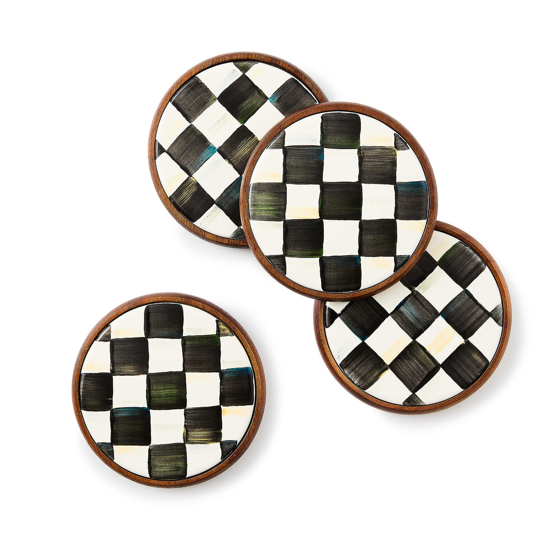 Set of four round coasters with hand-painted black and white checkered plates in acacia wood bases.