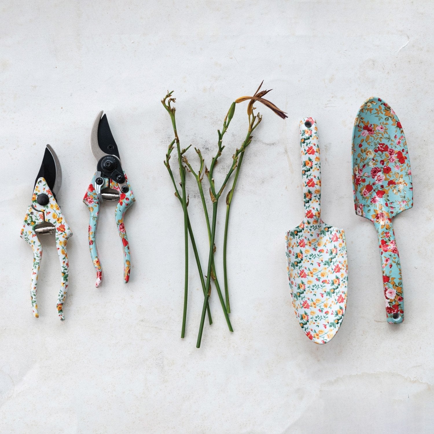 Floral patterned garden pruning shears and hand trowels displayed on a white surface.