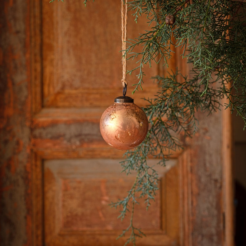 Cameo antique finished glass 3-inch ball ornament hanging from a twine string on a pine branch.