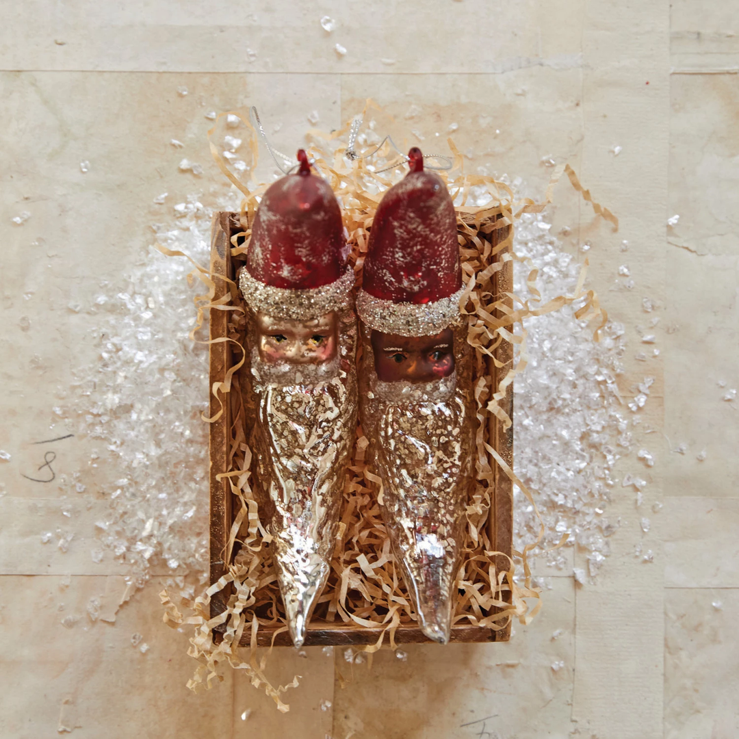 Two mercury glass Santa moon ornaments with red hats and glitter beards in a wooden box.