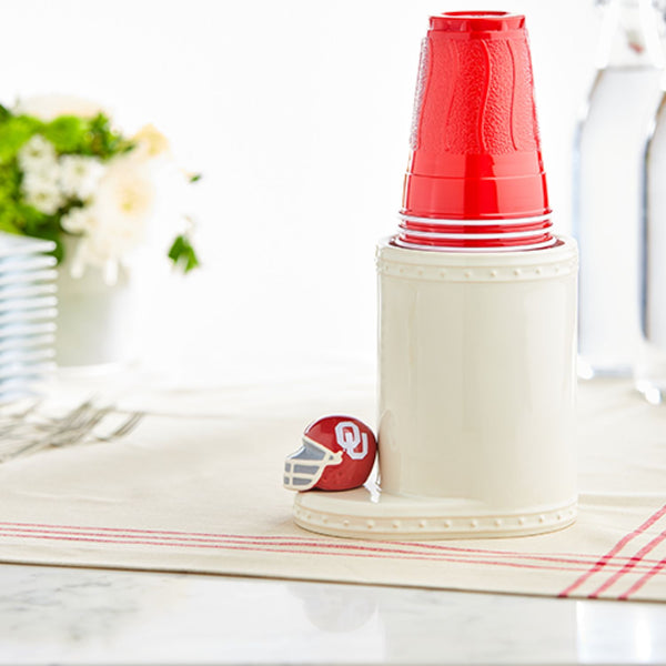 Nora Fleming Oklahoma University mini helmet on a white ceramic cup holder with red plastic cups.