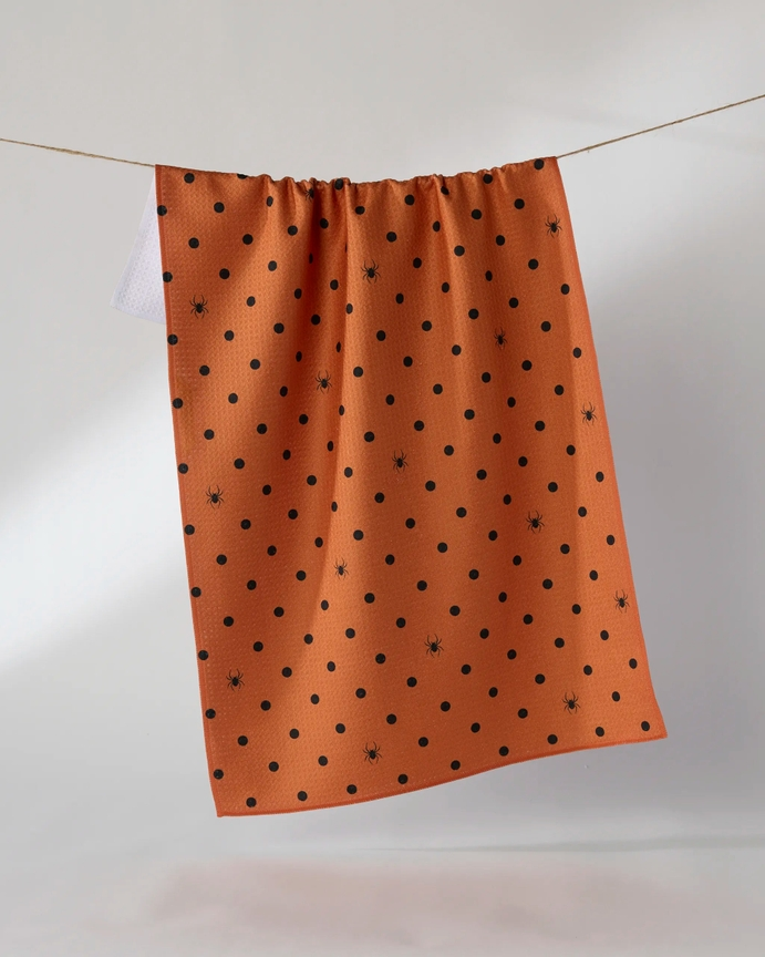 Orange waffle weave Halloween tea towel with black polka dots and spider patterns hanging on a line.