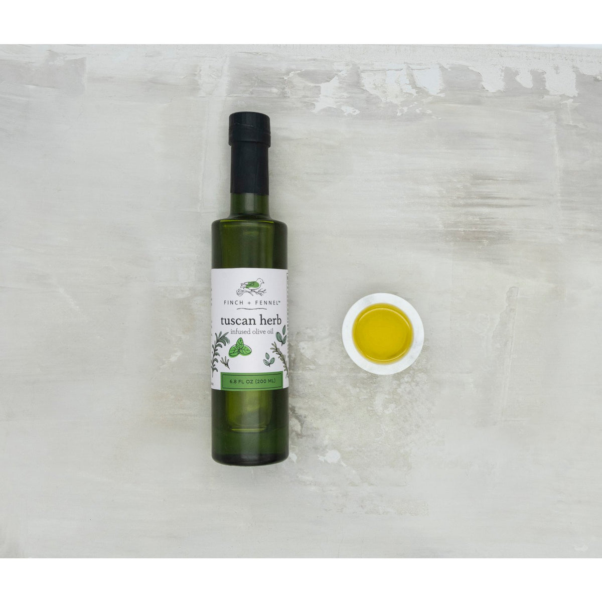 Bottle of Tuscan Herb Infused Olive Oil with a clear glass silhouette showing green liquid and herb flecks.